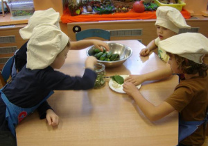 Dzieci wkładają do słoików ogórki i przyprawy.
